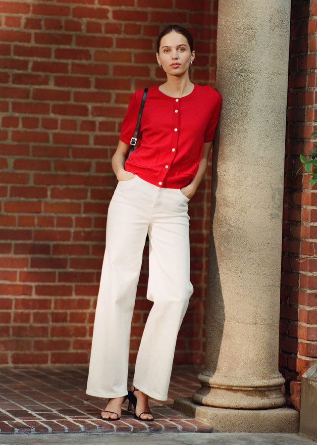 Woman in a red shirt and white pants leaning against a column with a brick wall background