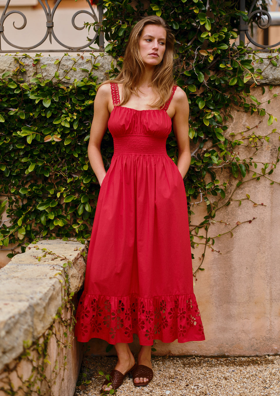 Woman in a red dress standing against a stone wall with greenery
