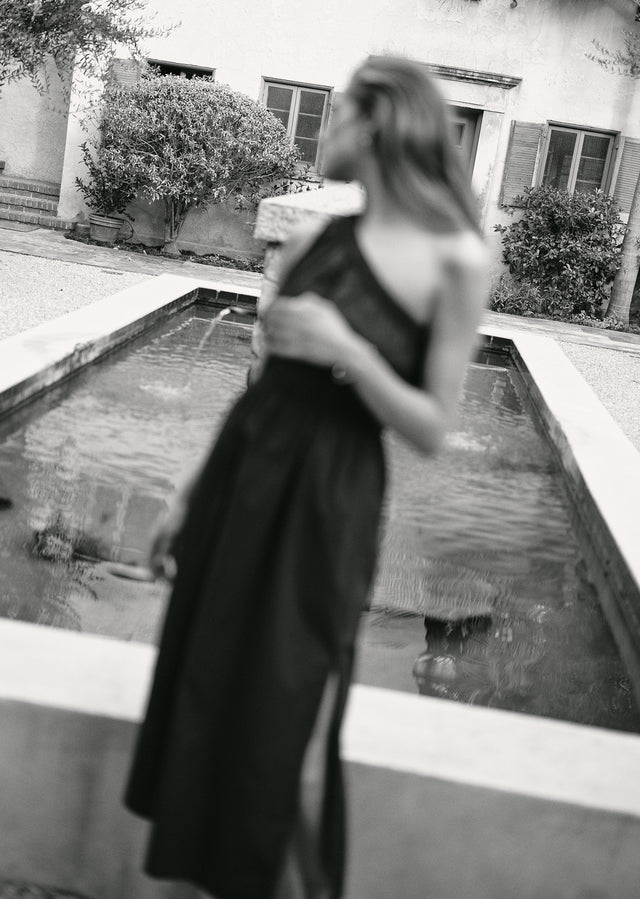 Woman in a black dress standing by a pool with a blurred background