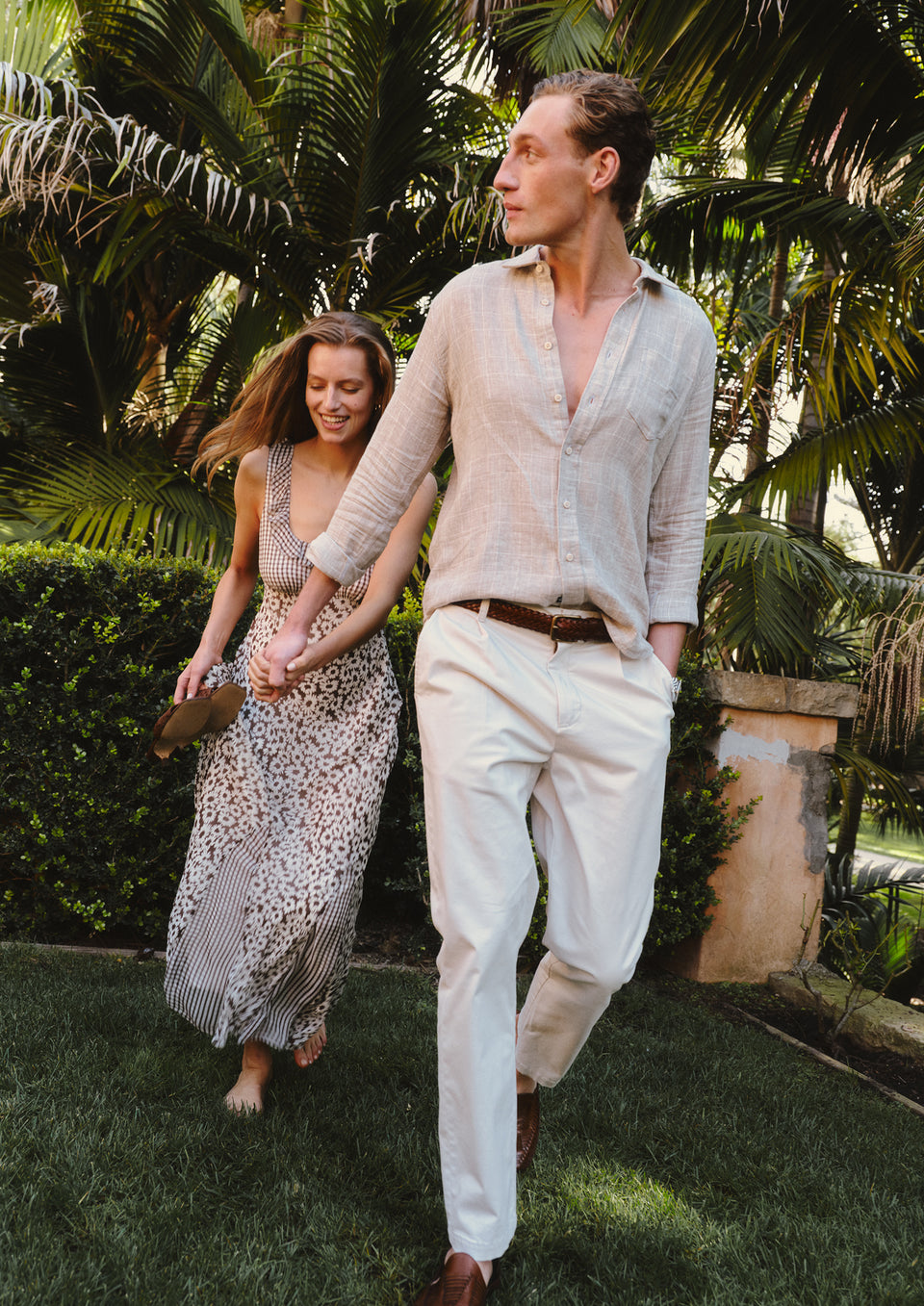 Man and woman walking together in a garden setting with tropical plants.