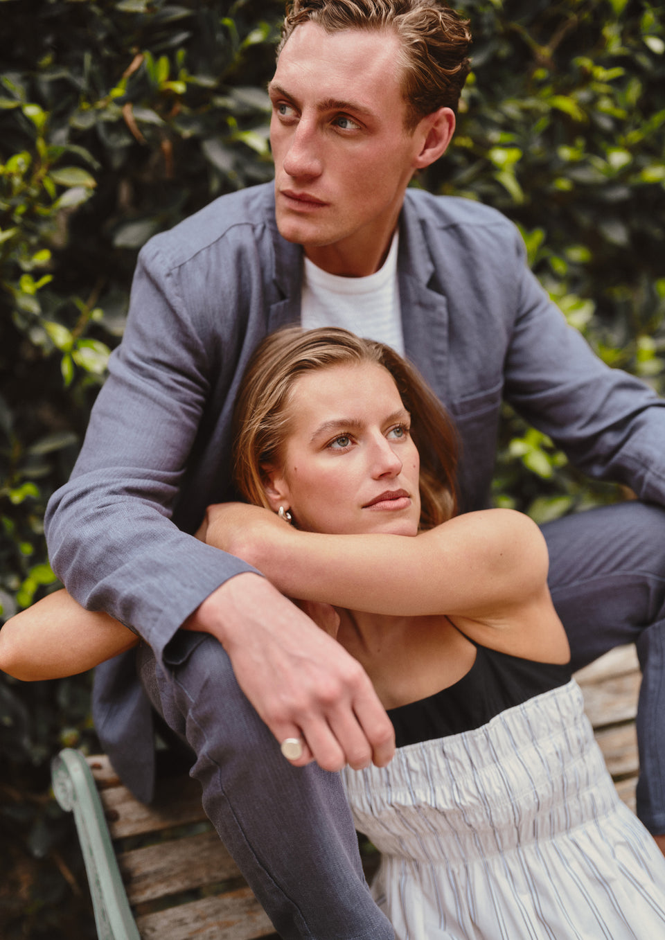 Two people sitting closely together outdoors with greenery in the background