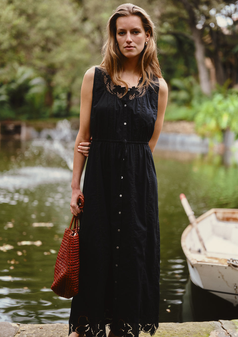 Woman in a black dress standing by a pond with boats in the background