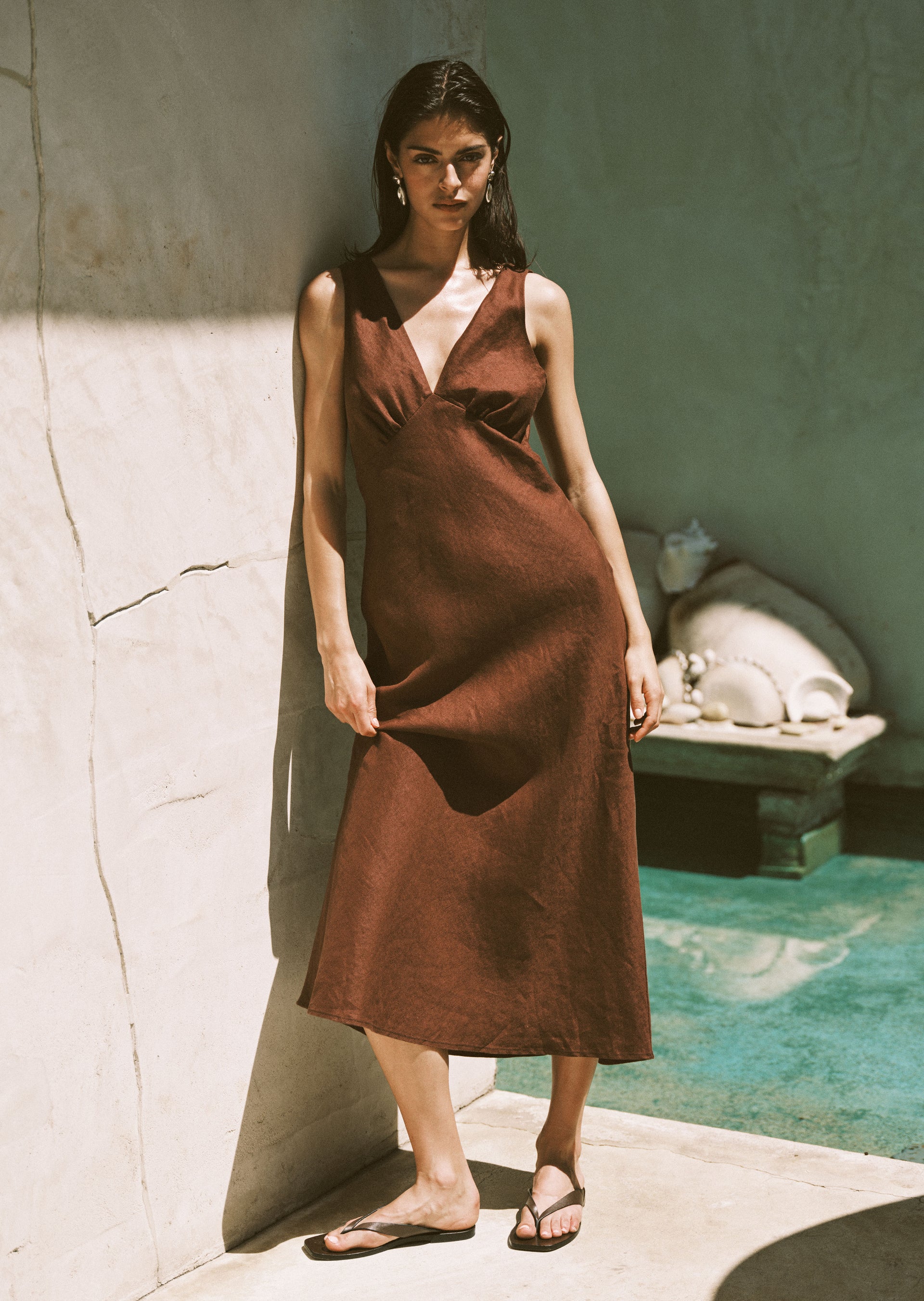 Woman in a brown dress standing by a poolside 