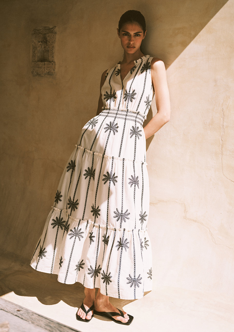 Woman wearing a white dress with black patterns against a beige wall.