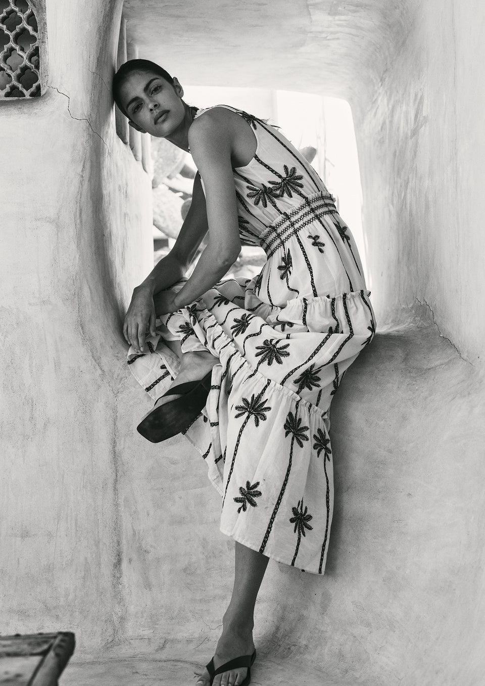 Woman in a patterned dress sitting on a stone wall.