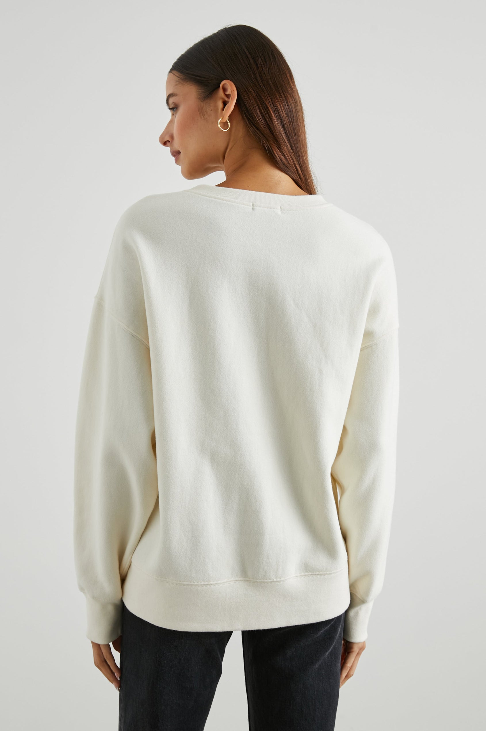 Cosmic Country Club Long-Sleeve Sweatshirt with a Crew Neck and the Front Black Text, Cosmic Country Club, Palm Springs, Rails and Friends 2010, and an Image of a Striped Setting Sun in Orange and Black in Winter White Colorway - Back View Featured on Model  