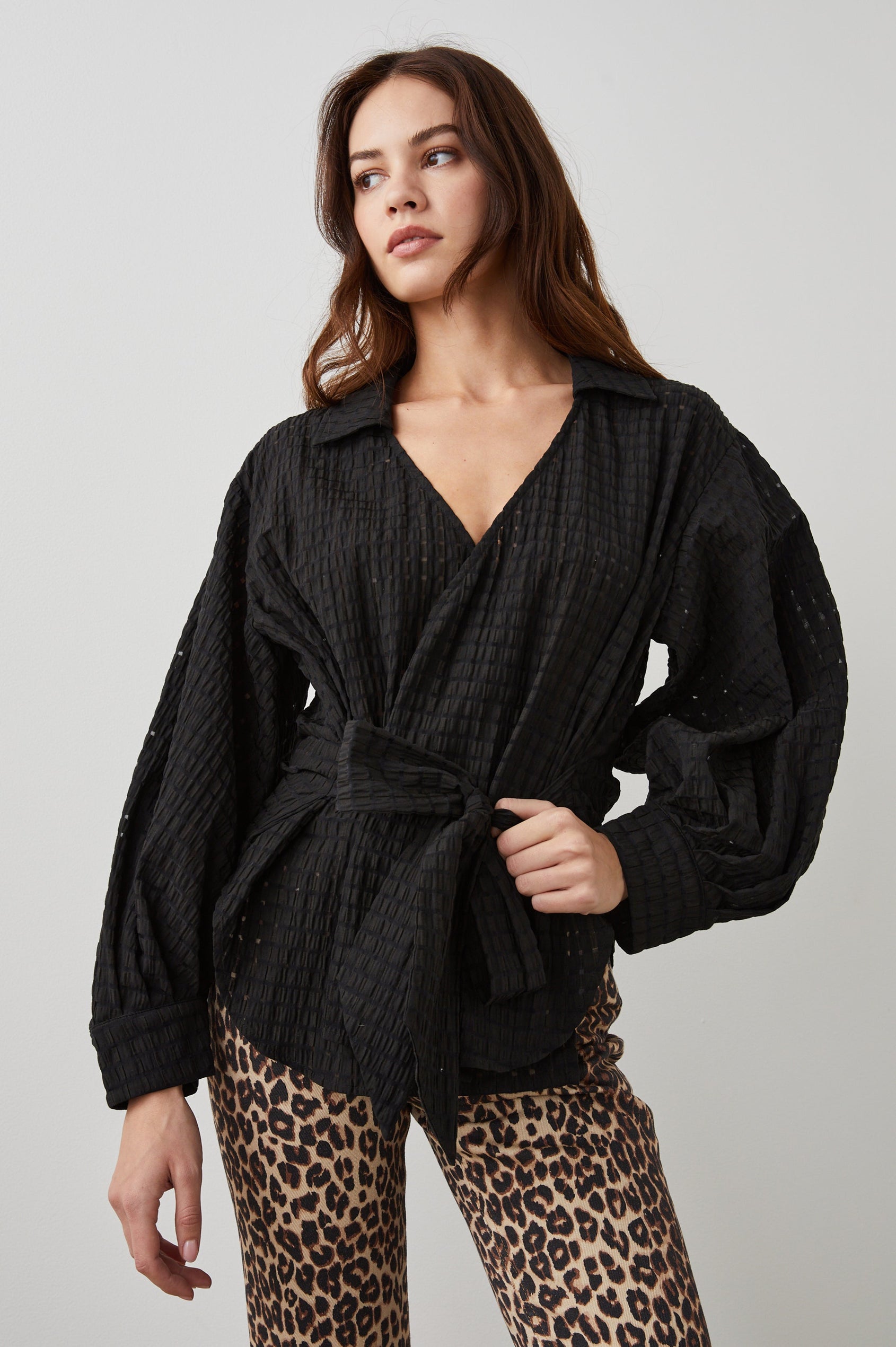 Eileen Long-Sleeve Wrap Top with Textured Fabric, a Deep V Neck, a Collar, a Wrap Tie at the Waist, Billowy Sleeves, in Black Seersucker Colorway - Front View Featured on Model 