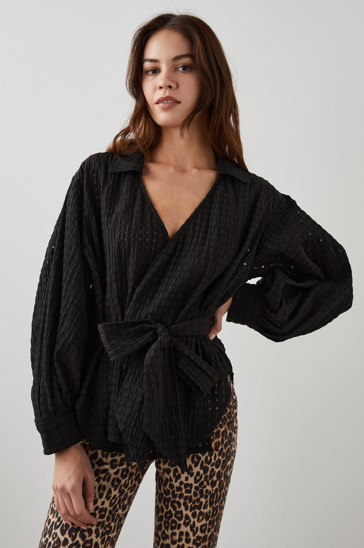 Eileen Long-Sleeve Wrap Top with Textured Fabric, a Deep V Neck, a Collar, a Wrap Tie at the Waist, Billowy Sleeves, in Black Seersucker Colorway - Front View Featured on Model 
