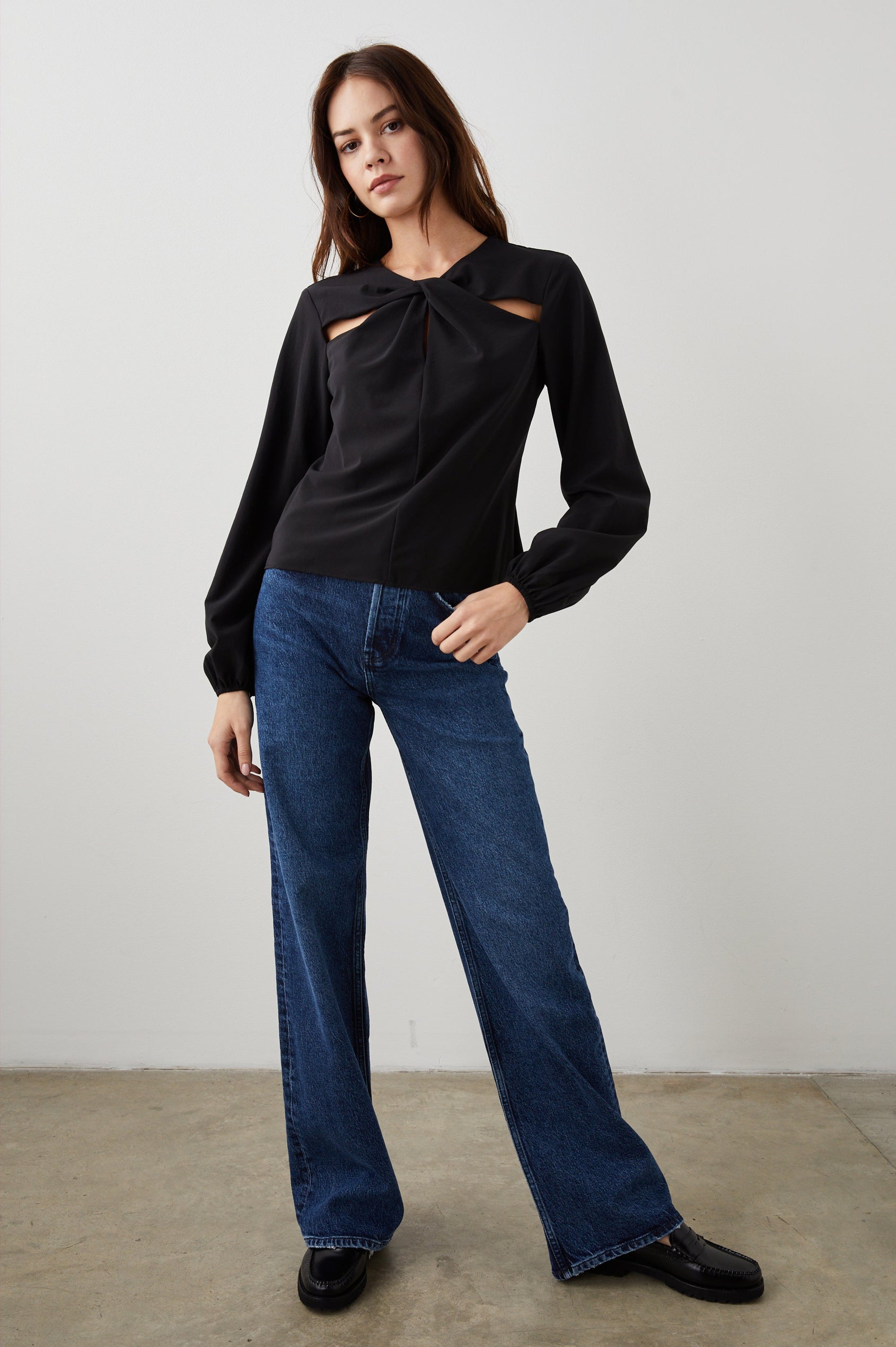 Eli Long-Sleeve Top with Twisted Fabric at the Neckline and a Cutout to the Left and Right of the Twist, a Vertical Seam Down the Front and a Keyhole at the Back in Black Colorway - Front Full Body View Featured on Model 