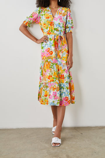 Eliana Midi Dress with Elbow-Length Sleeves with Shirred Cuffs, a V Neck, Buttons Down the Bodice, a Fabric Tie at the Waist  and a Tiered Skirt in Day Garden Colorway, a Floral Pattern in Blue, Pink and Oranges on White - Front Full Body View Featured on Model