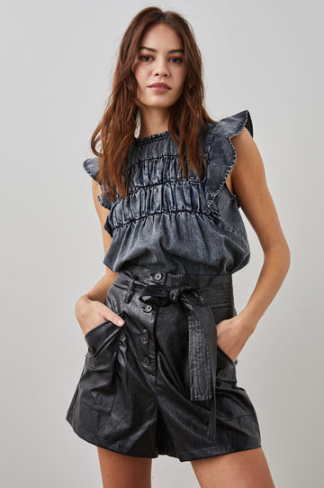 Filomena Short Sleeve Denim Top with Flutter Sleeves, a Ruffled Neck, a Shirred Center Bodice, Lace Inserts and a Buttoned Keyhole at the Back in Ink Wash Colorway - Front Tucked View Featured on Model