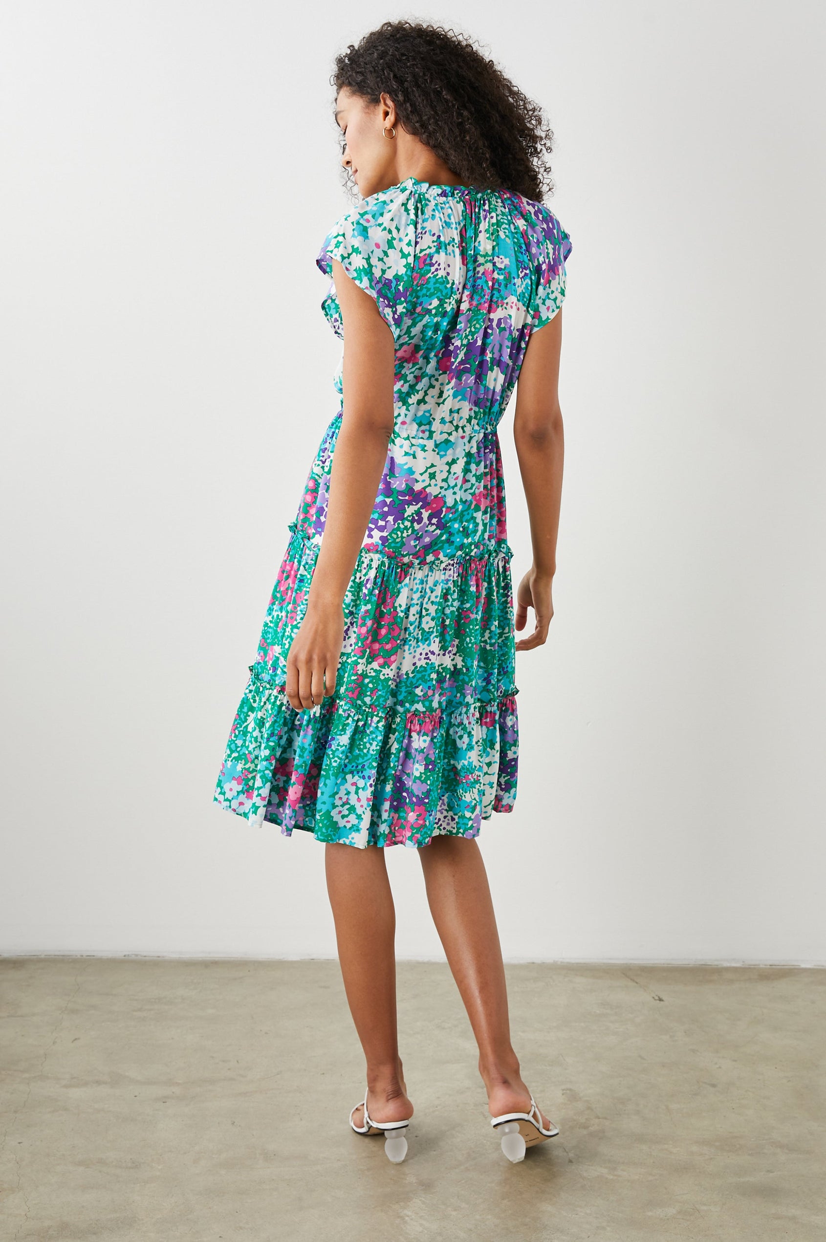 Juni Short Sleeve Midi Dress with a V Neck, Light Ruching along the Neckline, a Drawstring Waist, and a Tiered Skirt in Gardenia Floral Colorway, in Greens, Blues, Purples, Pinks and White - Back Full Body View Featured on Model