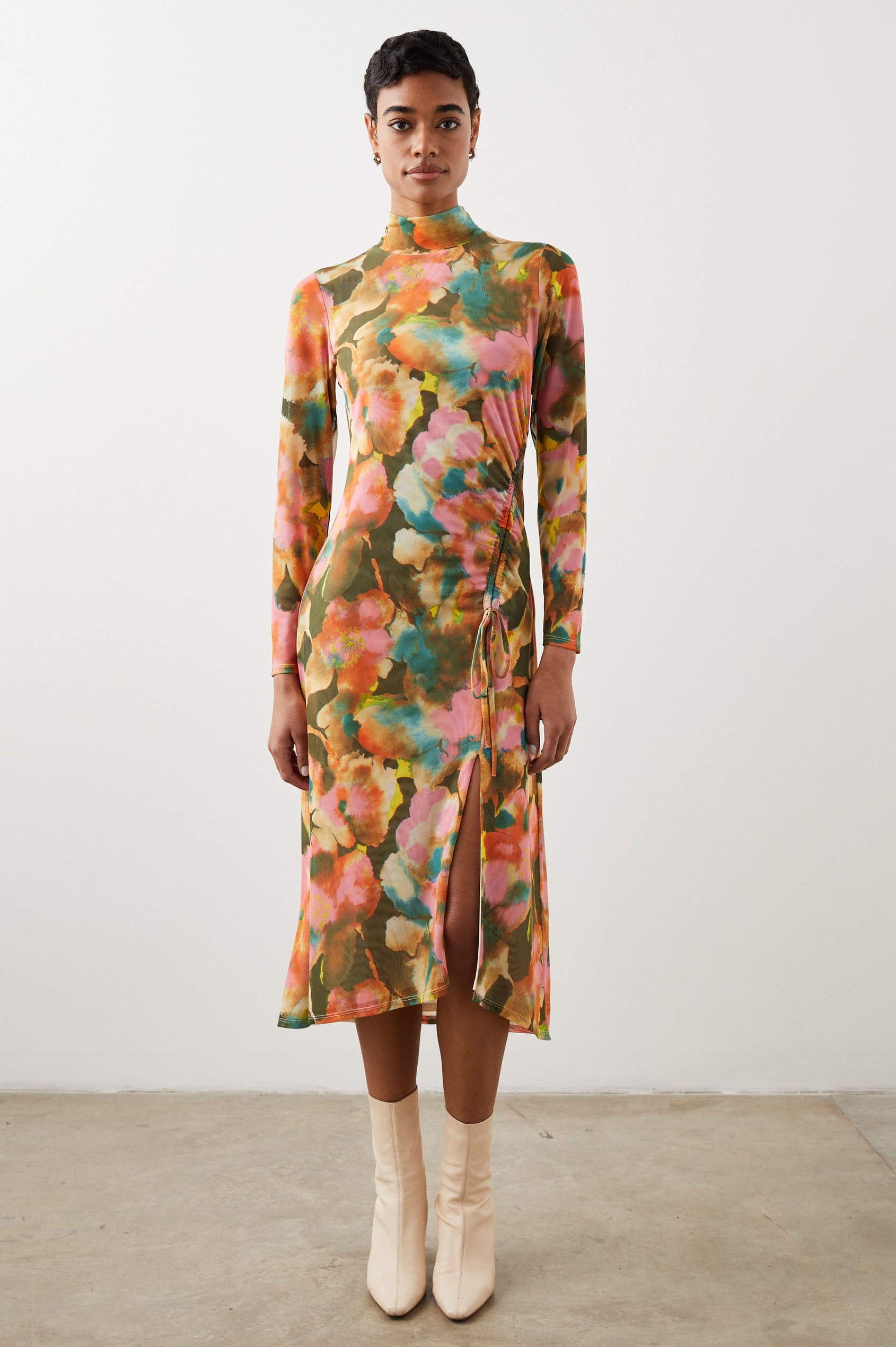 Mona Long Sleeve Midi Dress with a Mock Neck, a Side Slit and Adjustable Ruching along the Left Side with a Drawstring in Terra Floral Colorway, Flowers in Pinks, Browns, Yellows and Blues on Olive - Front Full Body View Featured on Model 