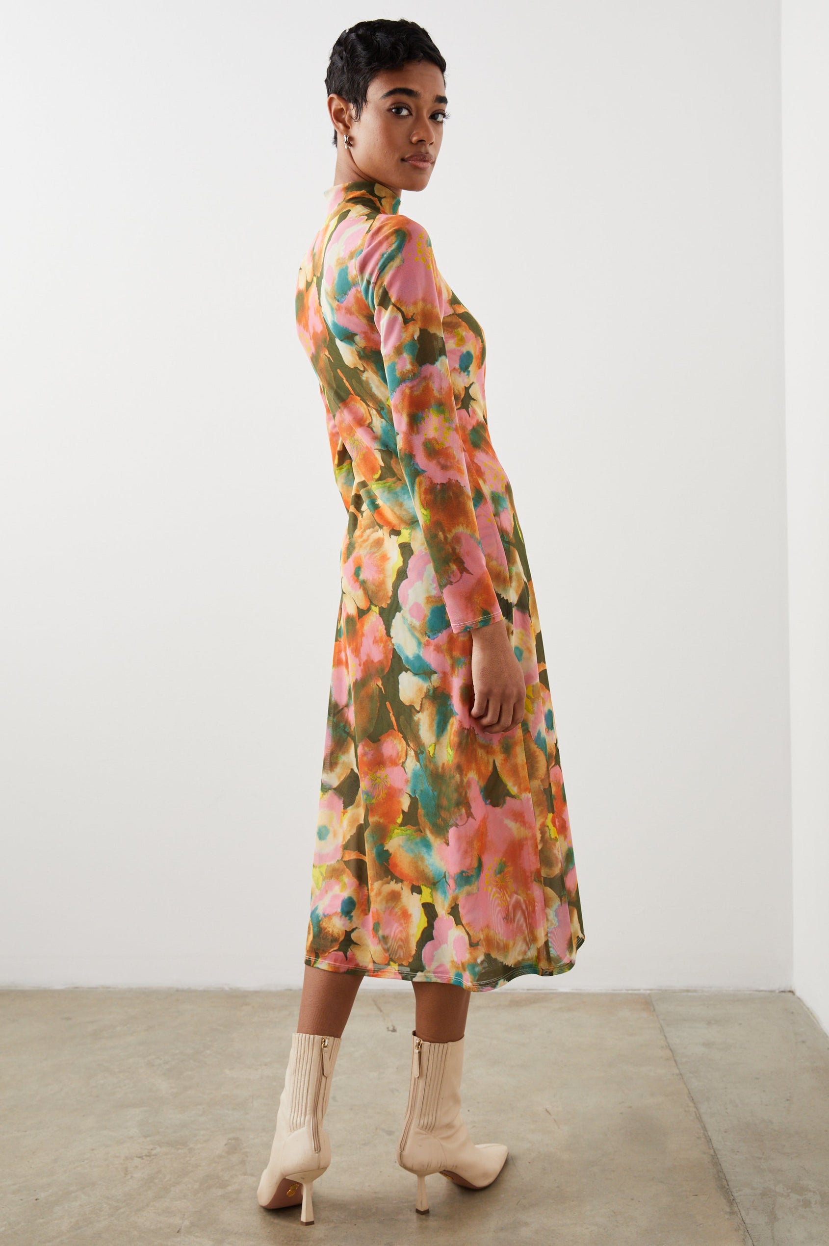 Mona Long Sleeve Midi Dress with a Mock Neck, a Side Slit and Adjustable Ruching along the Left Side with a Drawstring in Terra Floral Colorway, Flowers in Pinks, Browns, Yellows and Blues on Olive - Back Full Body View Featured on Model 