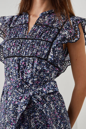 Sofie Short Sleeve Midi Dress with Flutter Sleeves, a V Neck, Panels with Shirring on the Bodice, a Fabric Waist Tie, a Tiered Skirt, and Cutouts on the Sleeves and Along the Hem in Midnight Hyacinth Colorway, Small Flowers in Blues, Pinks and White on Midnight - Front View Featured on Model 